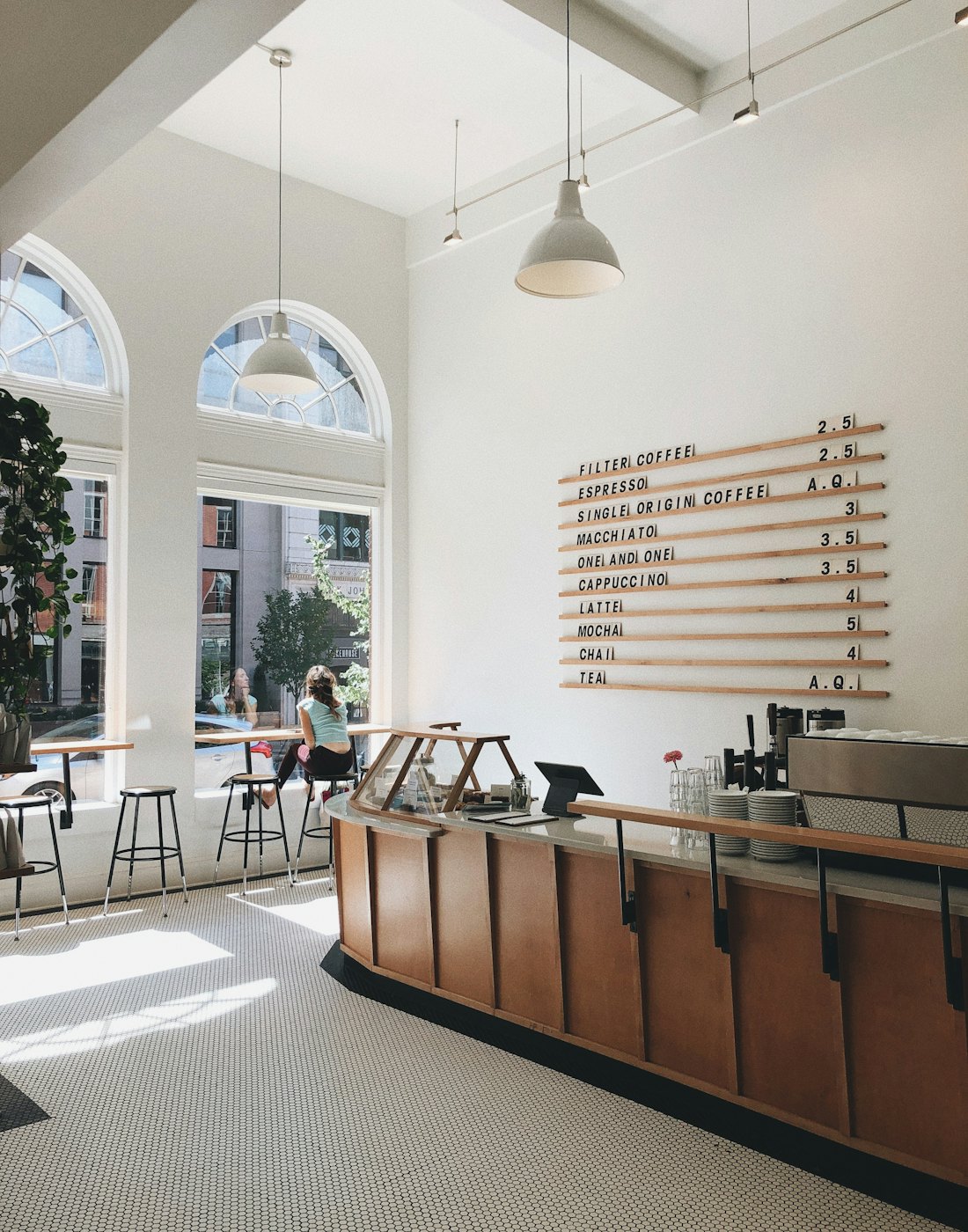 Sunlit café room with tall arched windows and a wooden bar