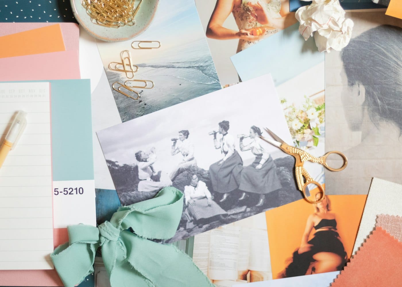 A mood board of photos, colour swatches, scissors and ribbon spread across a desk