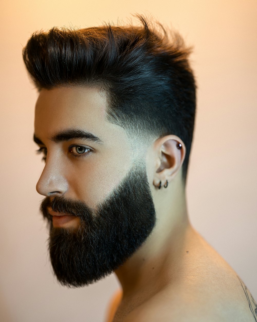 Skin fade kesimli, dolgun sakallı bir adamın yandan portresi