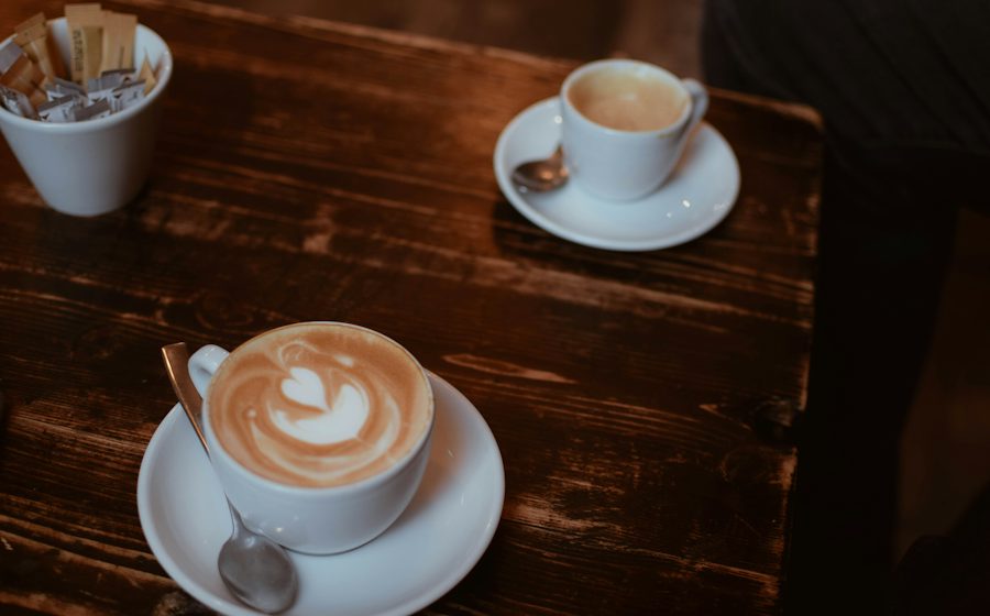 Koyu ahşap masada latte ve küçük bir kahve fincanı