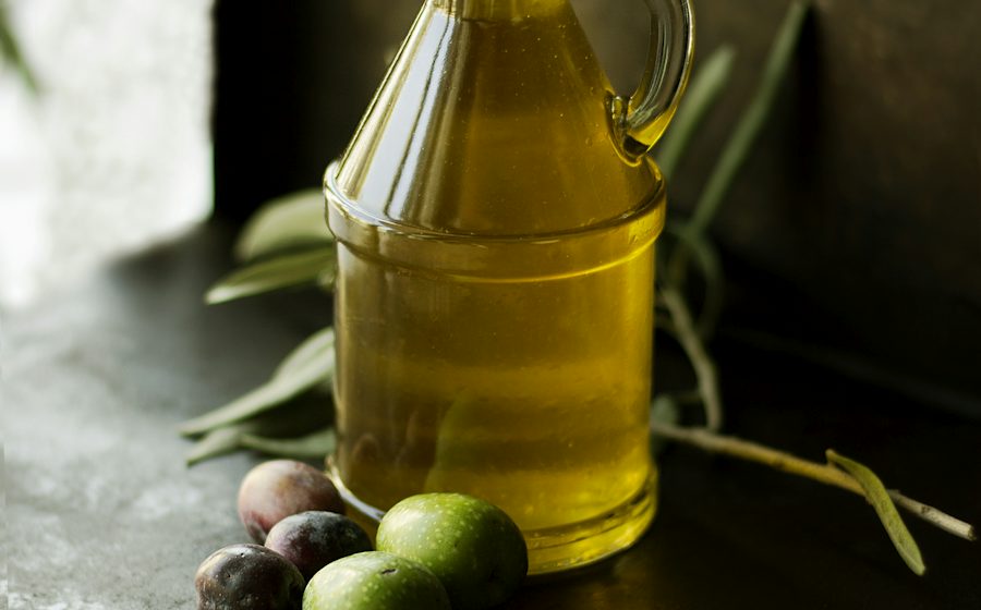 Karanlık zeminde zeytinyağı şişesi, taze zeytin ve limon
