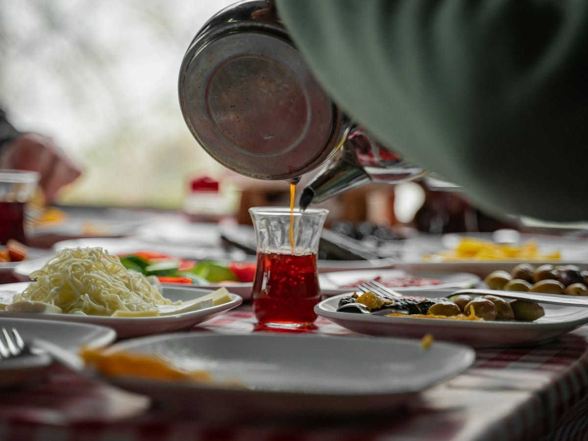 Tea being poured into a small glass over a breakfast table