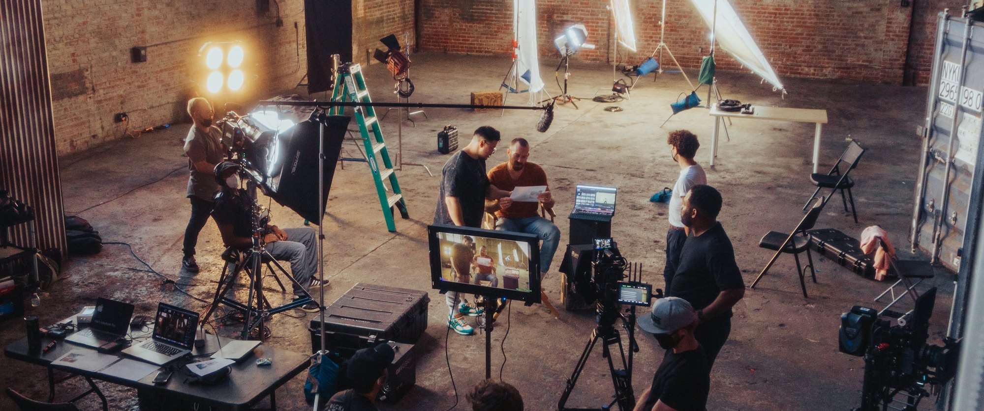 A film set built inside a brick warehouse, with cameras, lights and crew